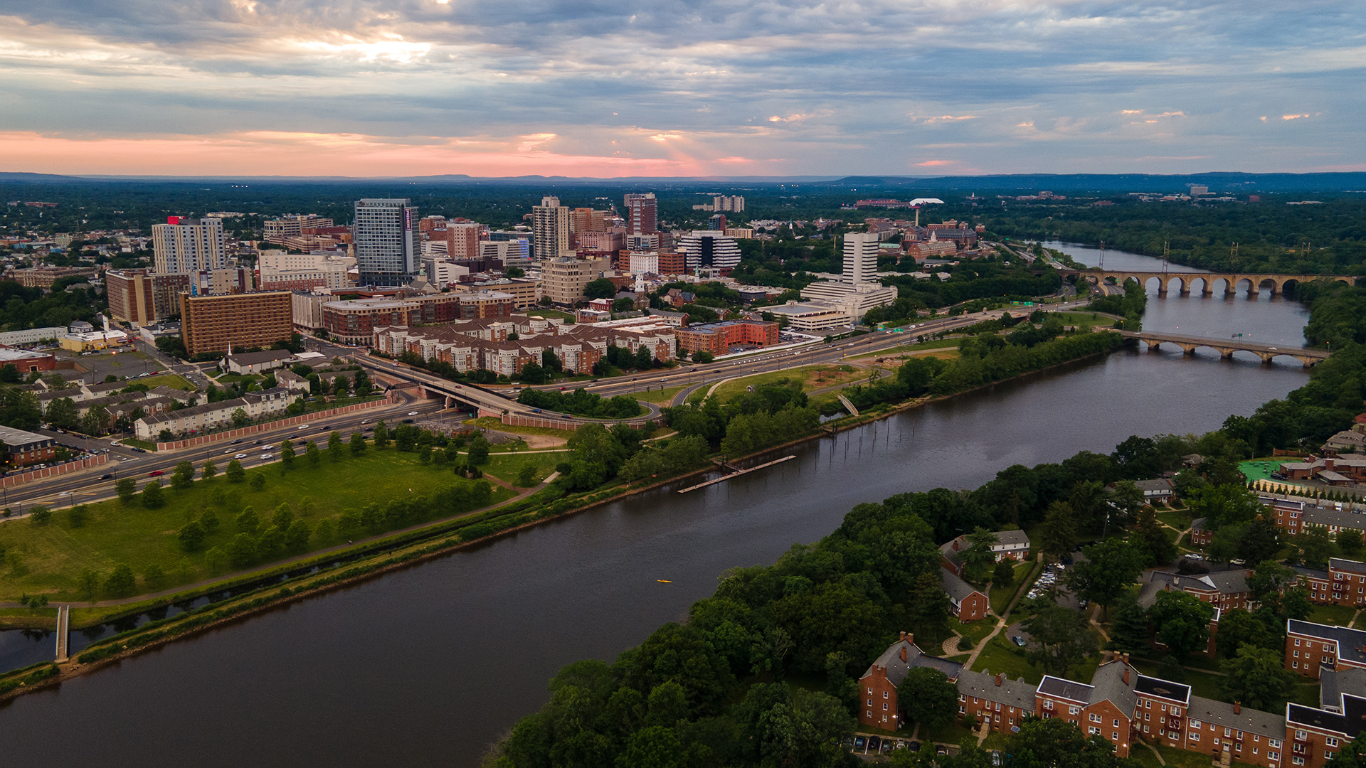 Aerial view of a city skyline with buildings, waterways, and a bridge at sunset.