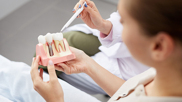 A dental professional examining a model mouth with various dental tools, set against a medical backdrop.